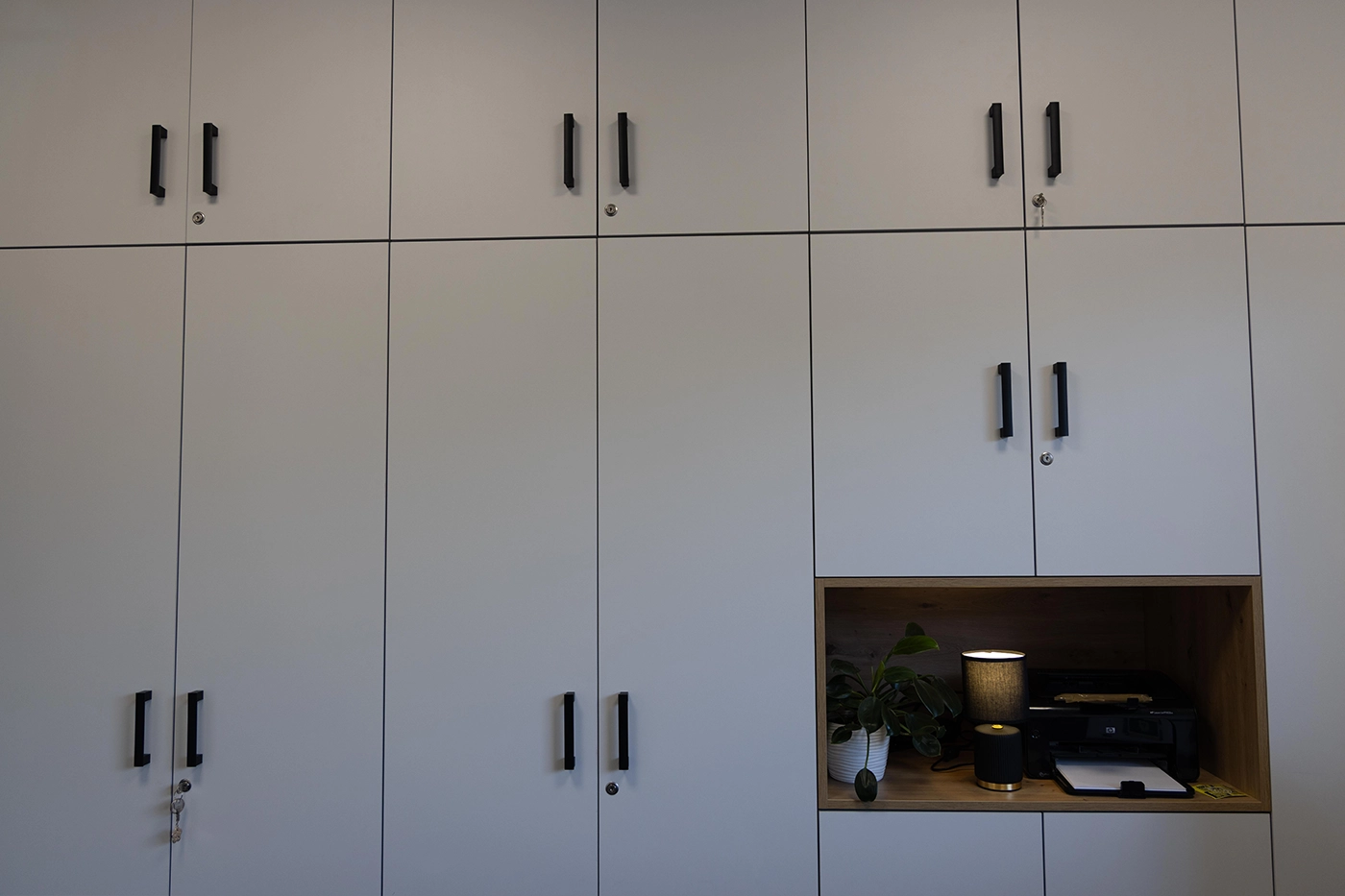 Szafy biurowe w zabudowie ściennej z matowymi frontami i uchwytami w kolorze czarnym