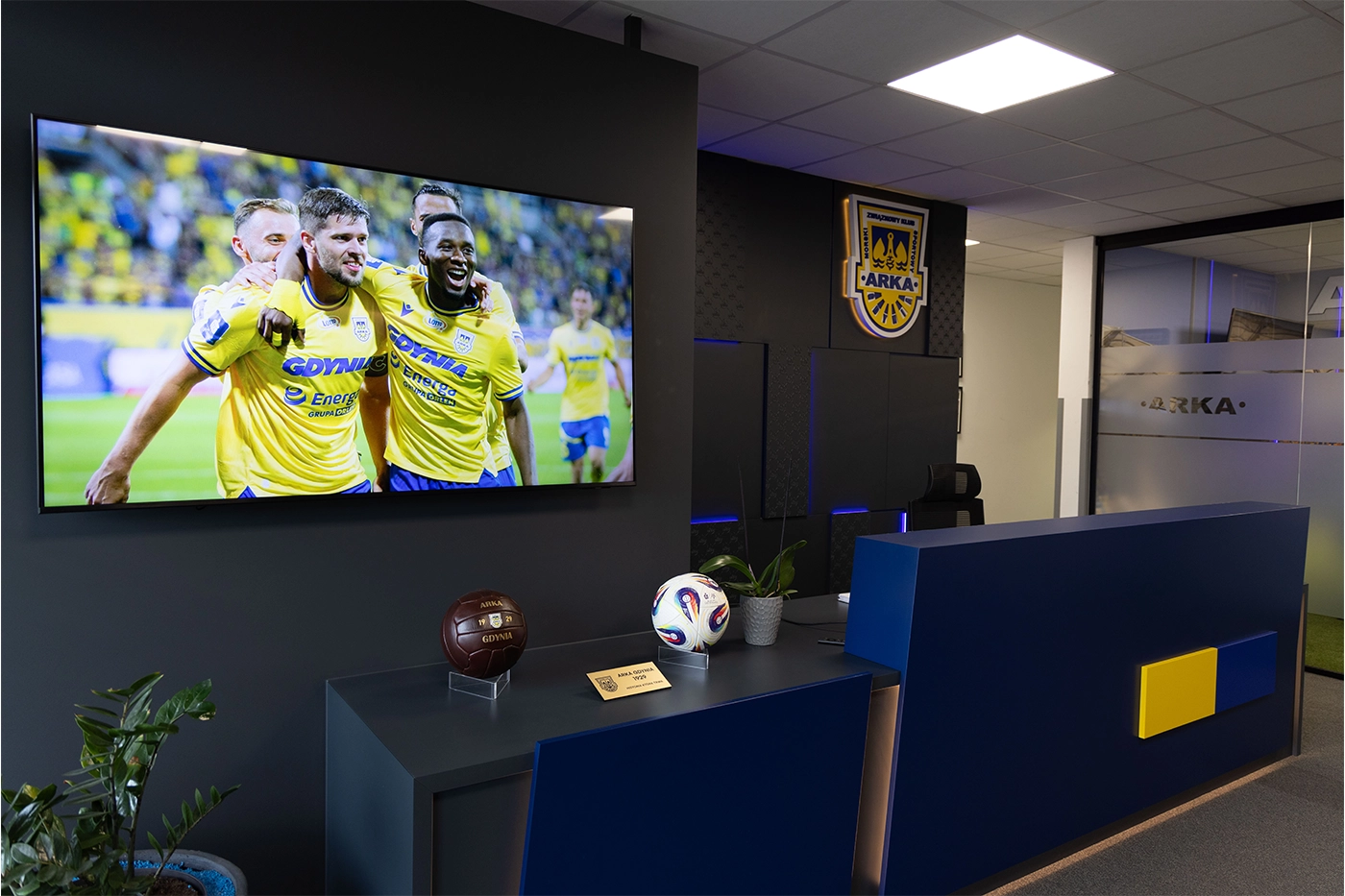 Podświetlane logo Arki Gdynia na ścianie w nowoczesnej zabudowie meblowej